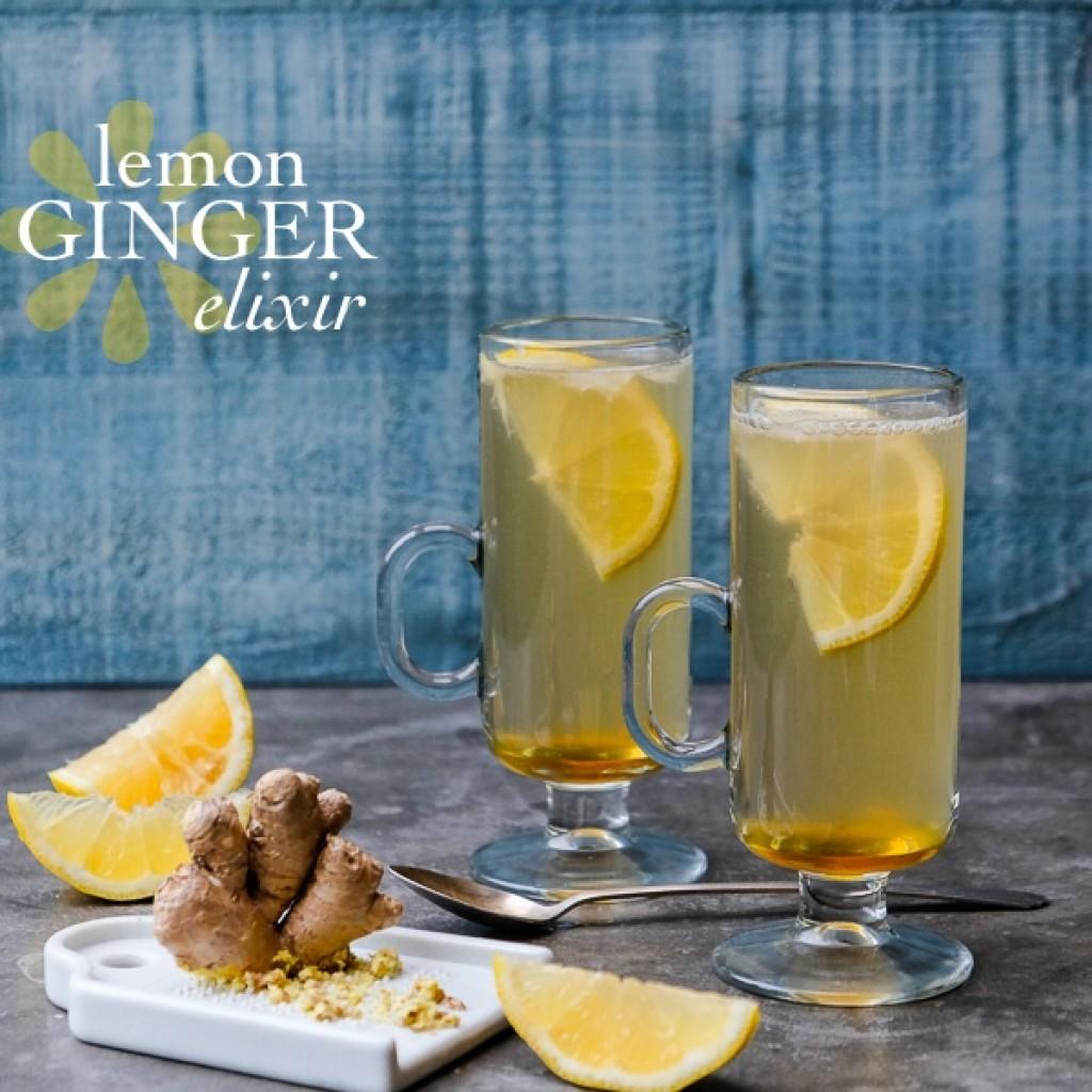 golden ginger elixir in a glass with sliced ginger and lemons around it