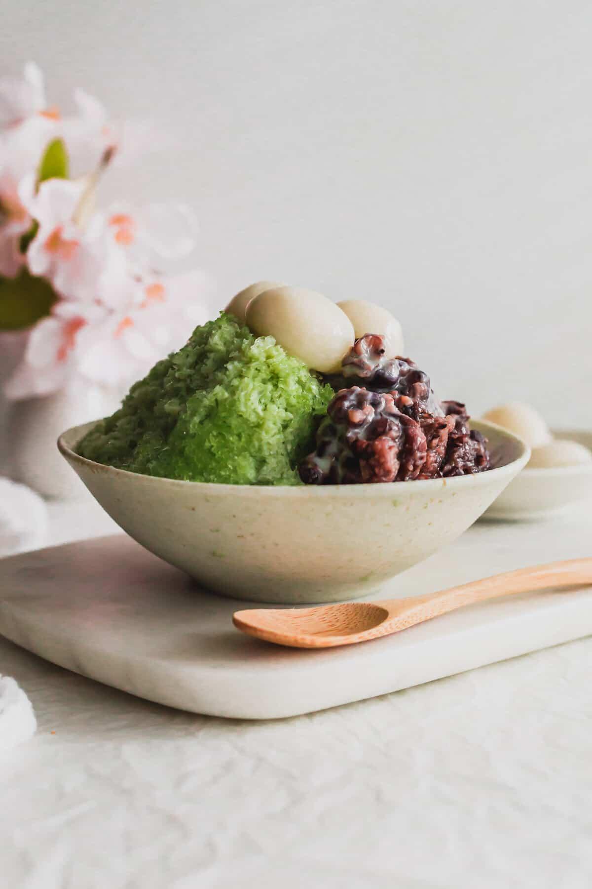 A bowl of green tea ice cream decorated with mochi, red bean paste, and edible flowers