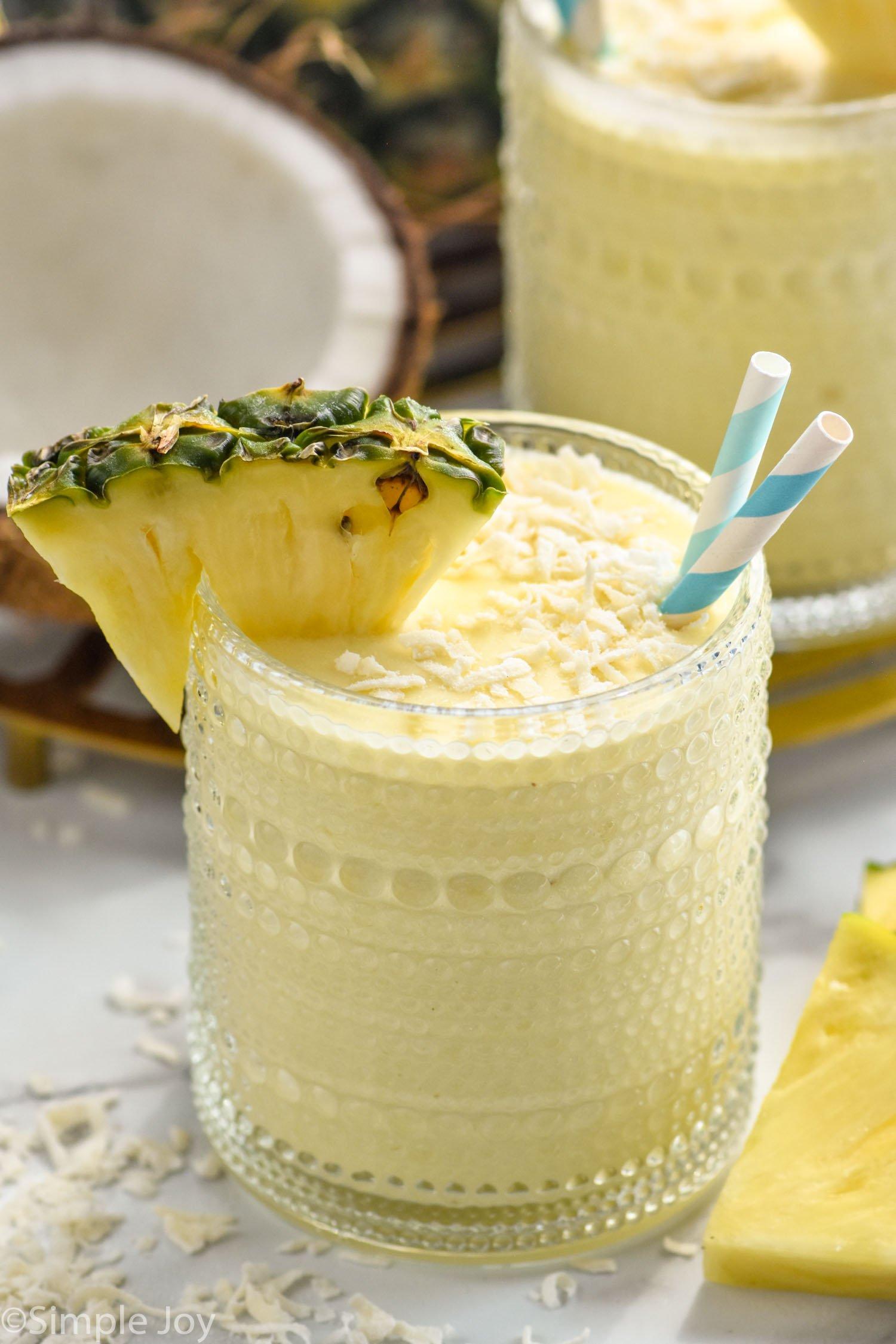 overhead shot of a bright yellow pina colada protein smoothie in a glass, garnished with a pineapple wedge and shredded coconut, on a white countertop
