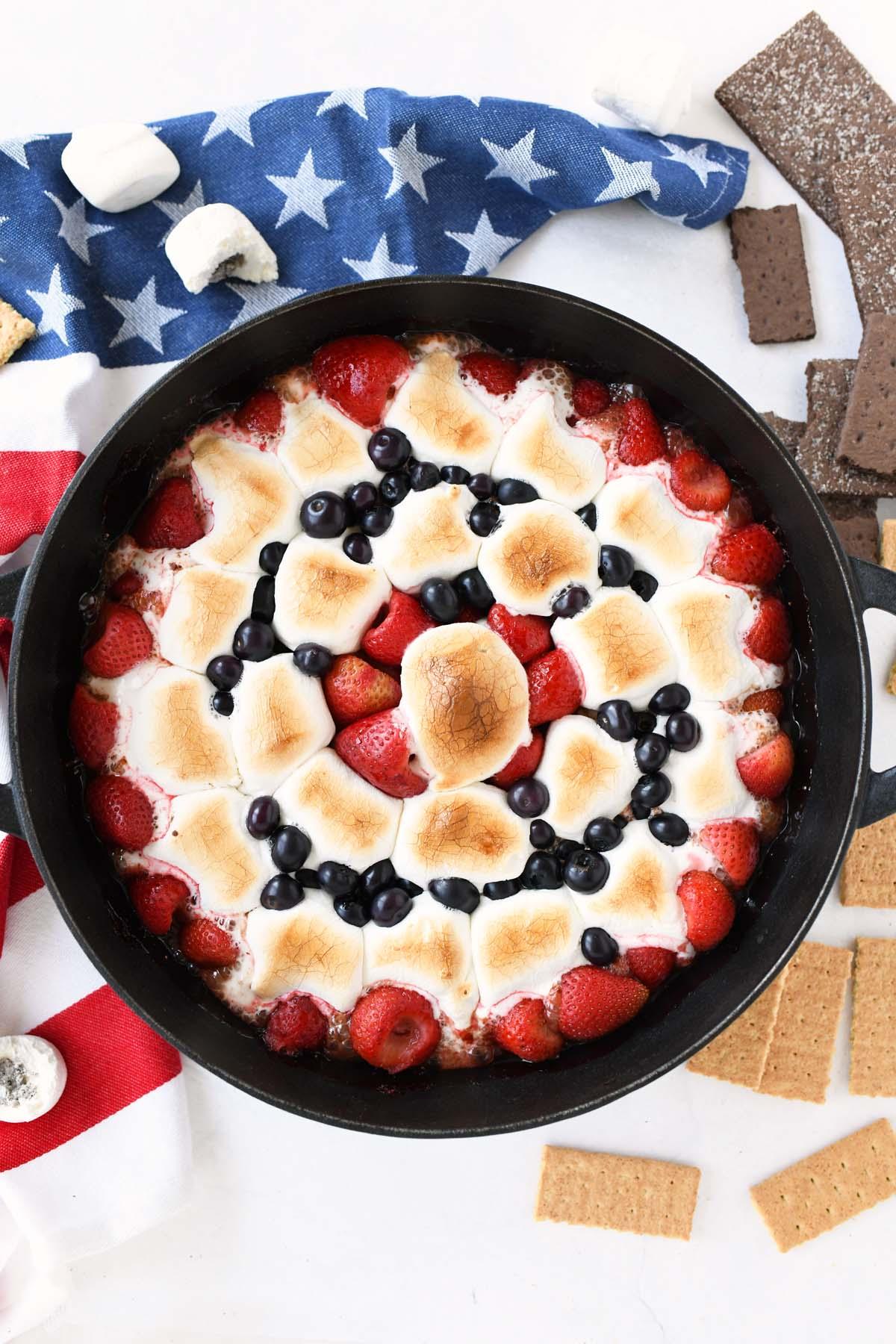 overhead shot of s'mores dip in a skillet with graham crackers, strawberries, blueberries, and raspberries arranged around it