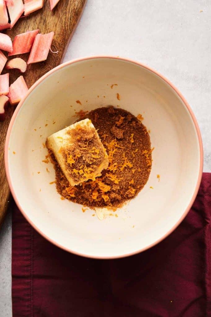 overhead shot of a whole rhubarb cake with cardamom and orange zest on a wooden cutting board