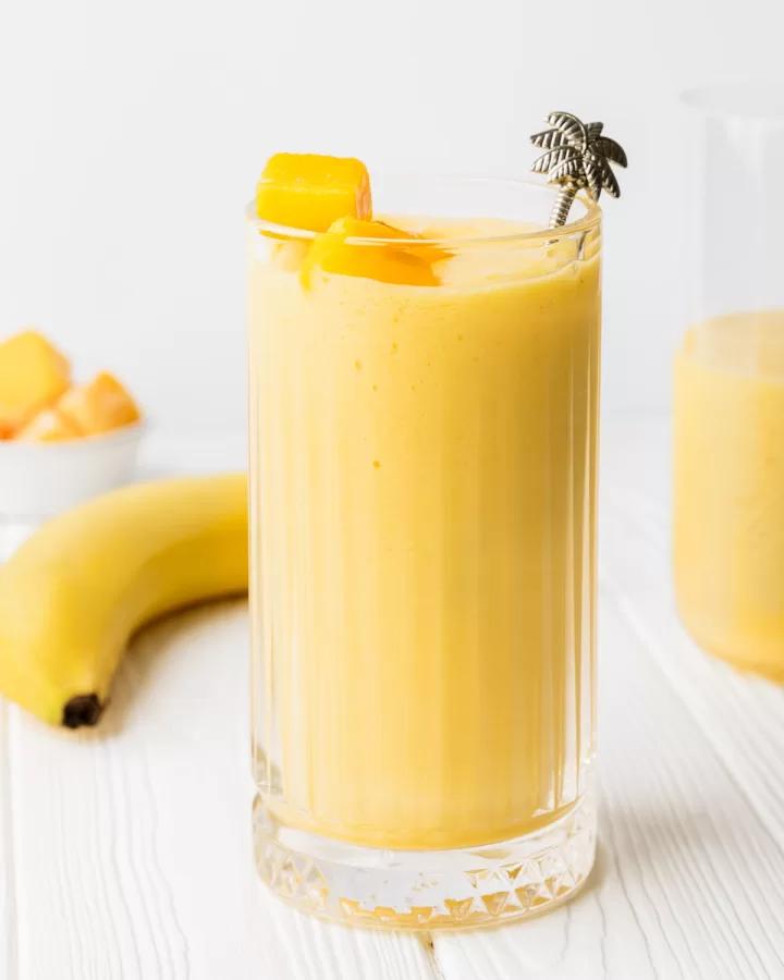 blended coconut mango protein smoothie in a glass with fresh mango pieces