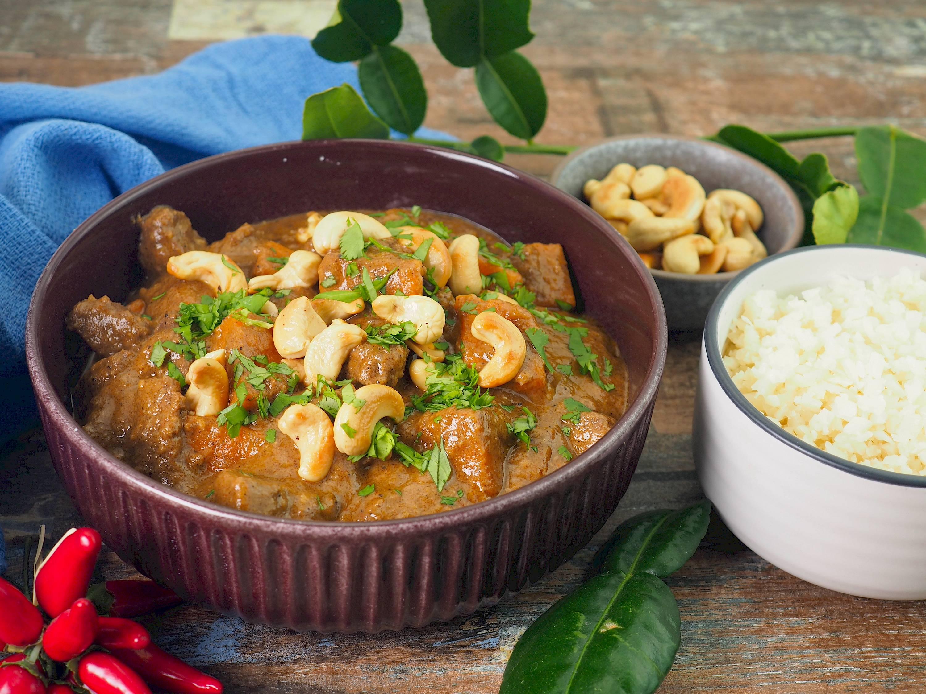 a person serving a bowl of macadamia nut massaman curry with rice and various garnishes