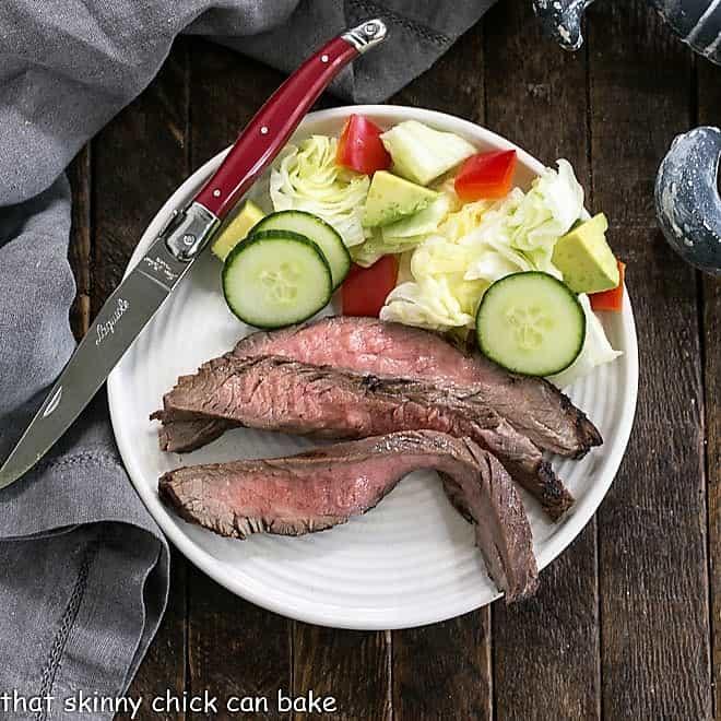 overhead shot of sliced flank steak on a white plate garnished with fresh herbs and orange slices
