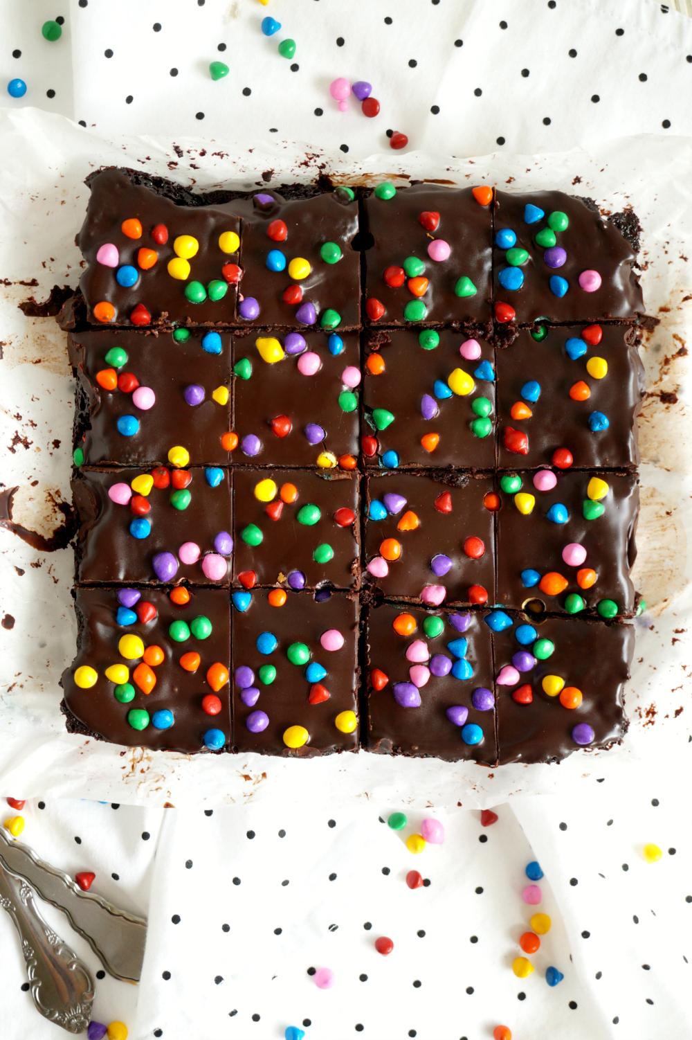 a hand sprinkling rainbow sprinkles on vegan brownies