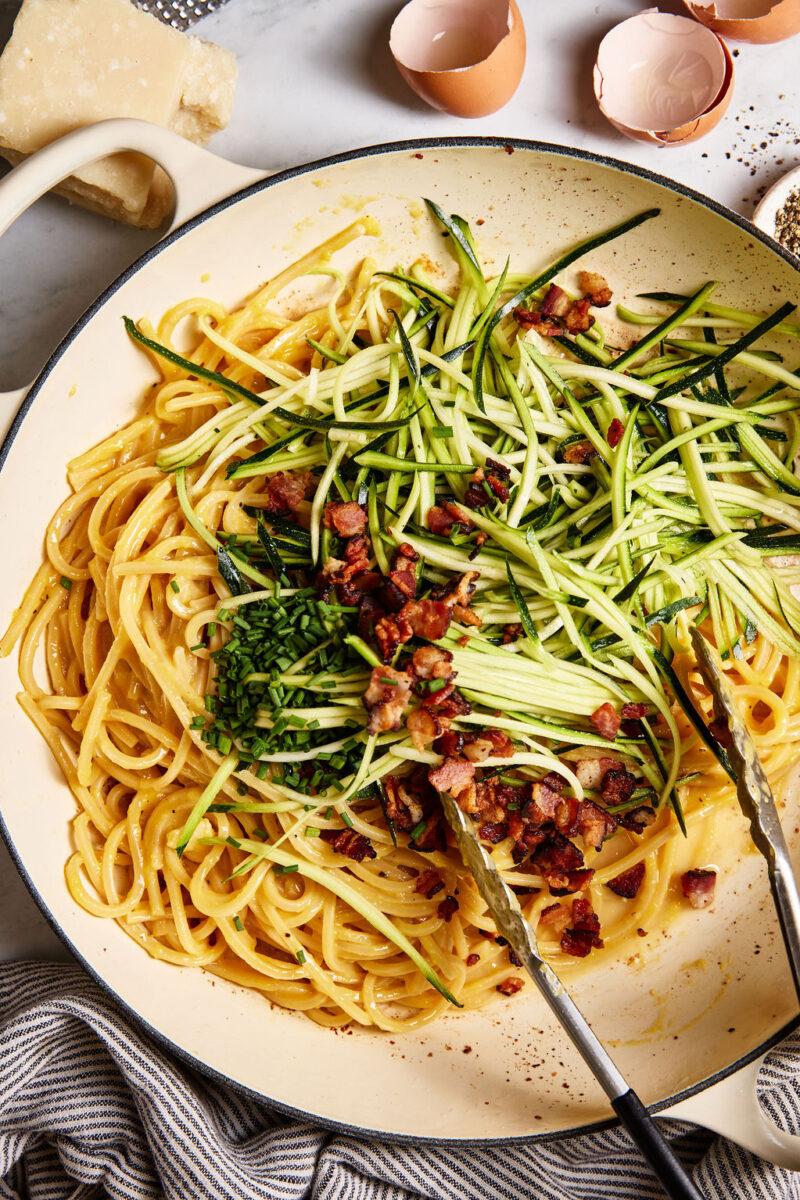 close up shot of crispy bacon being crumbled onto zucchini noodles