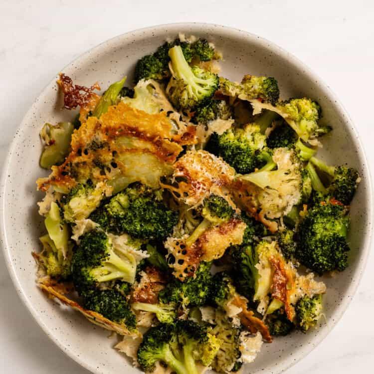 a bowl of vibrant green roasted broccoli with melted Parmesan cheese