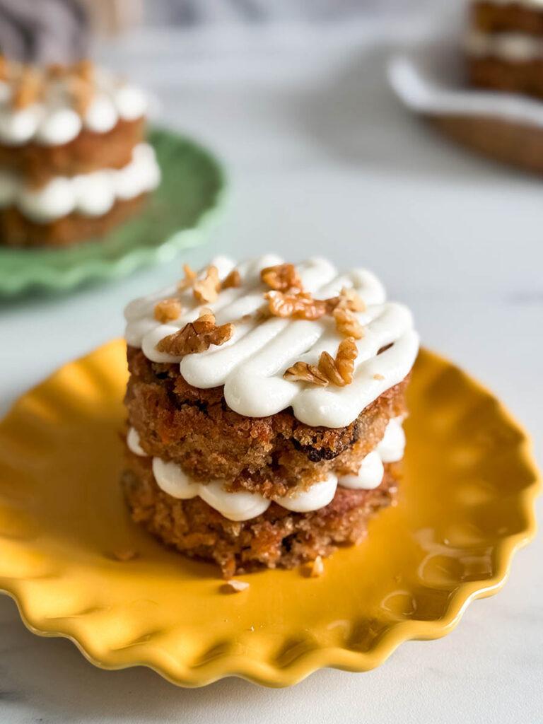 a hand holding a carrot cake mini cupcake, with more blurred in the background