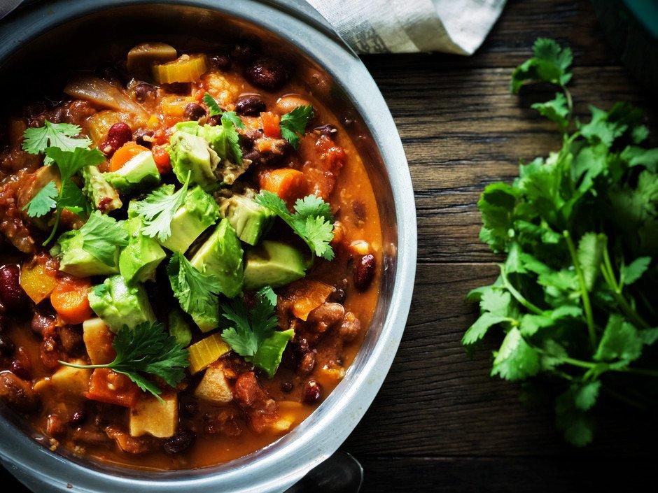 Close-up shot of a bowl of sweet potato and corn vegan chili garnished with avocado and cilantro
