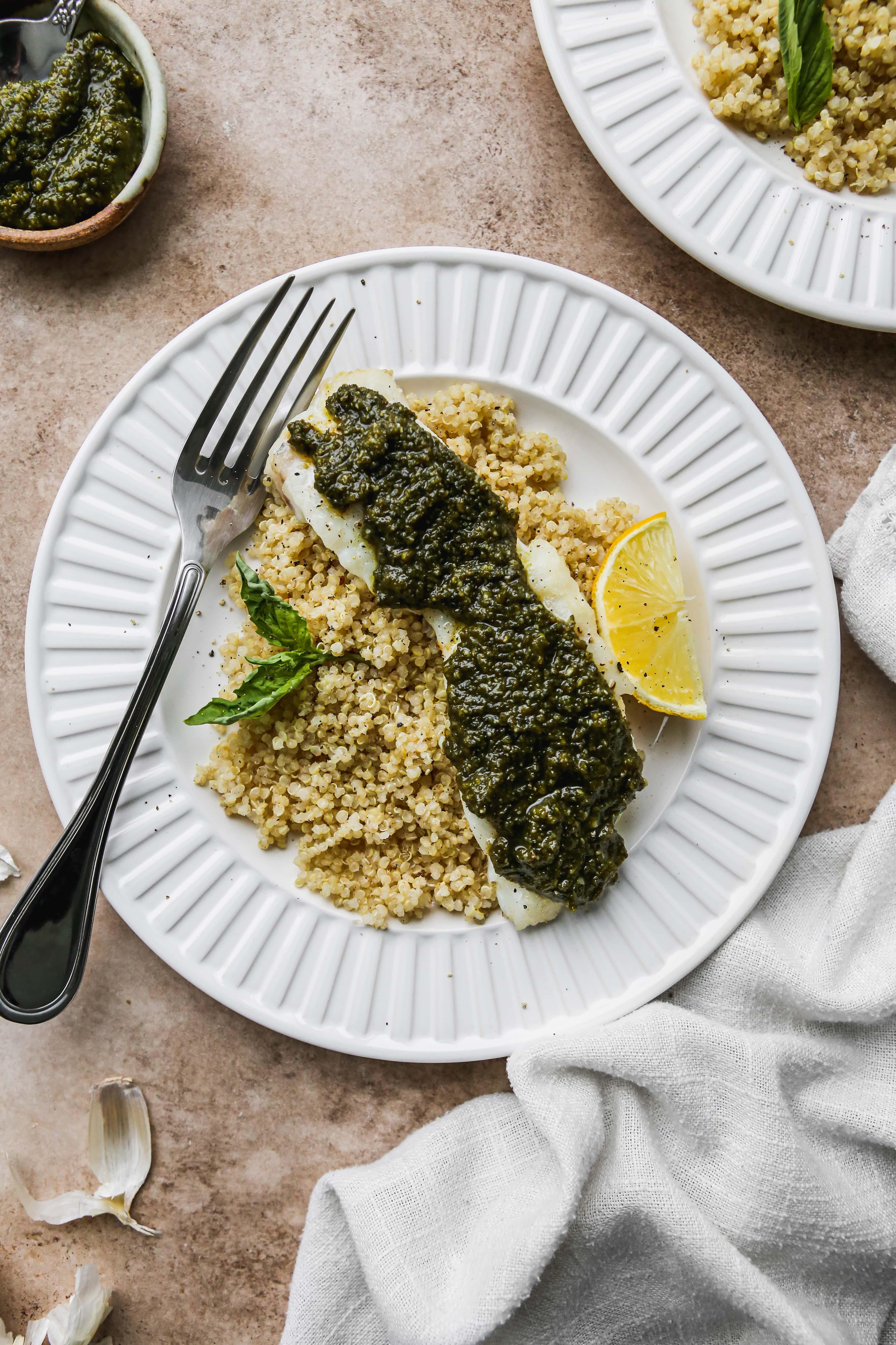 side view of grilled cod with pesto and pine nuts served on a plate