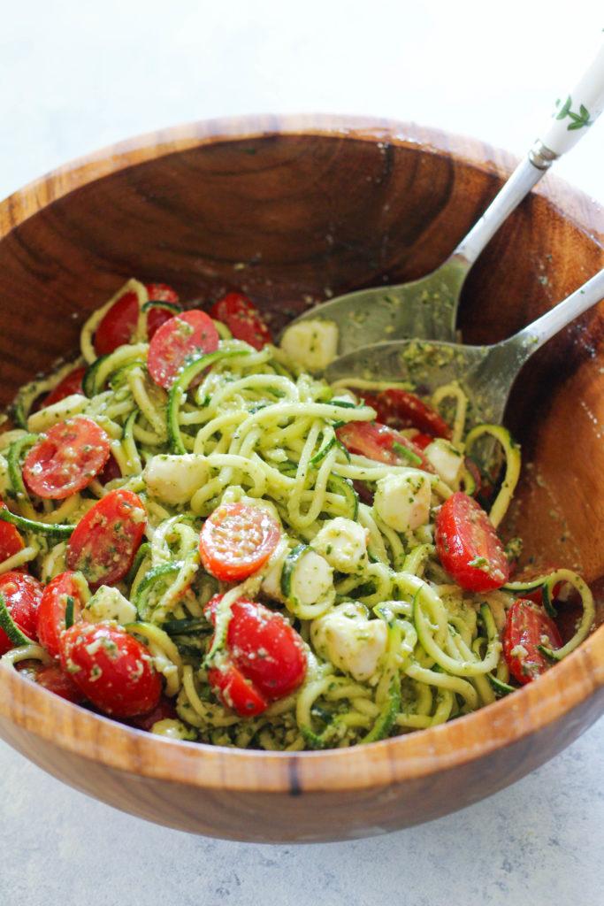 zucchini noodles being tossed with pesto in a bowl