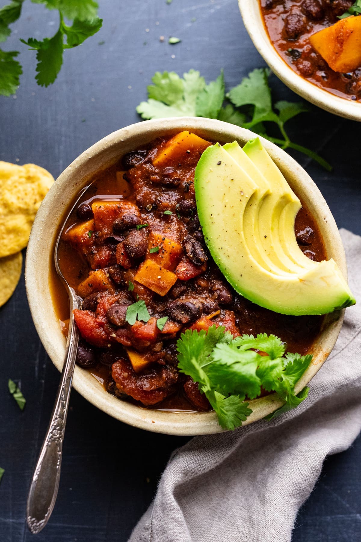 a steaming bowl of sweet potato and corn vegan chili topped with avocado