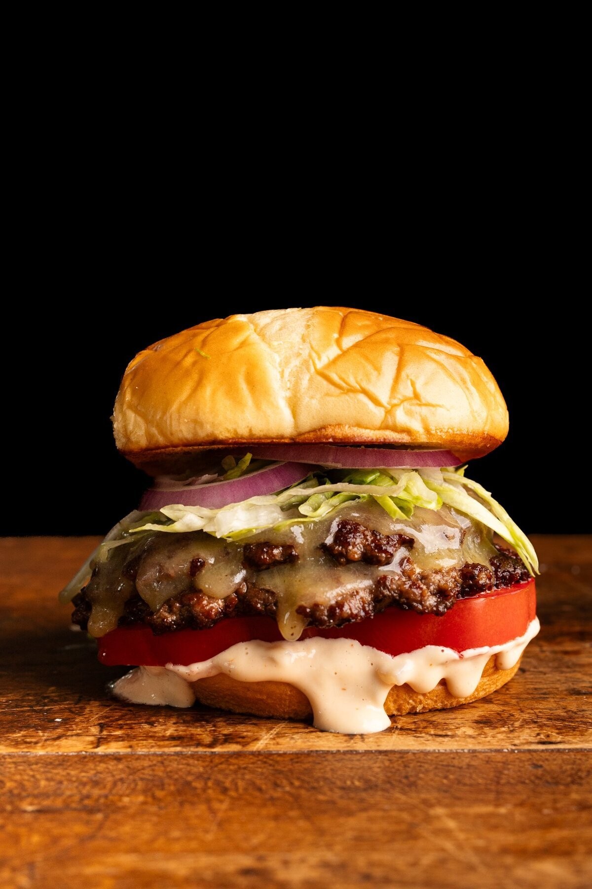 Delicious smash burger with melted cheese and secret sauce dripping, close-up, rustic wooden board