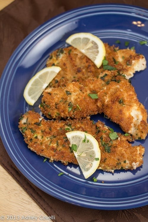 Skillet with crispy golden brown turkey cutlets, fresh herbs, lemon wedges