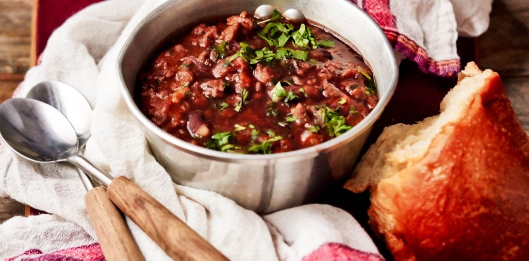rustic chili stew in a cast iron pot on a wooden table with crusty bread, cozy kitchen scene