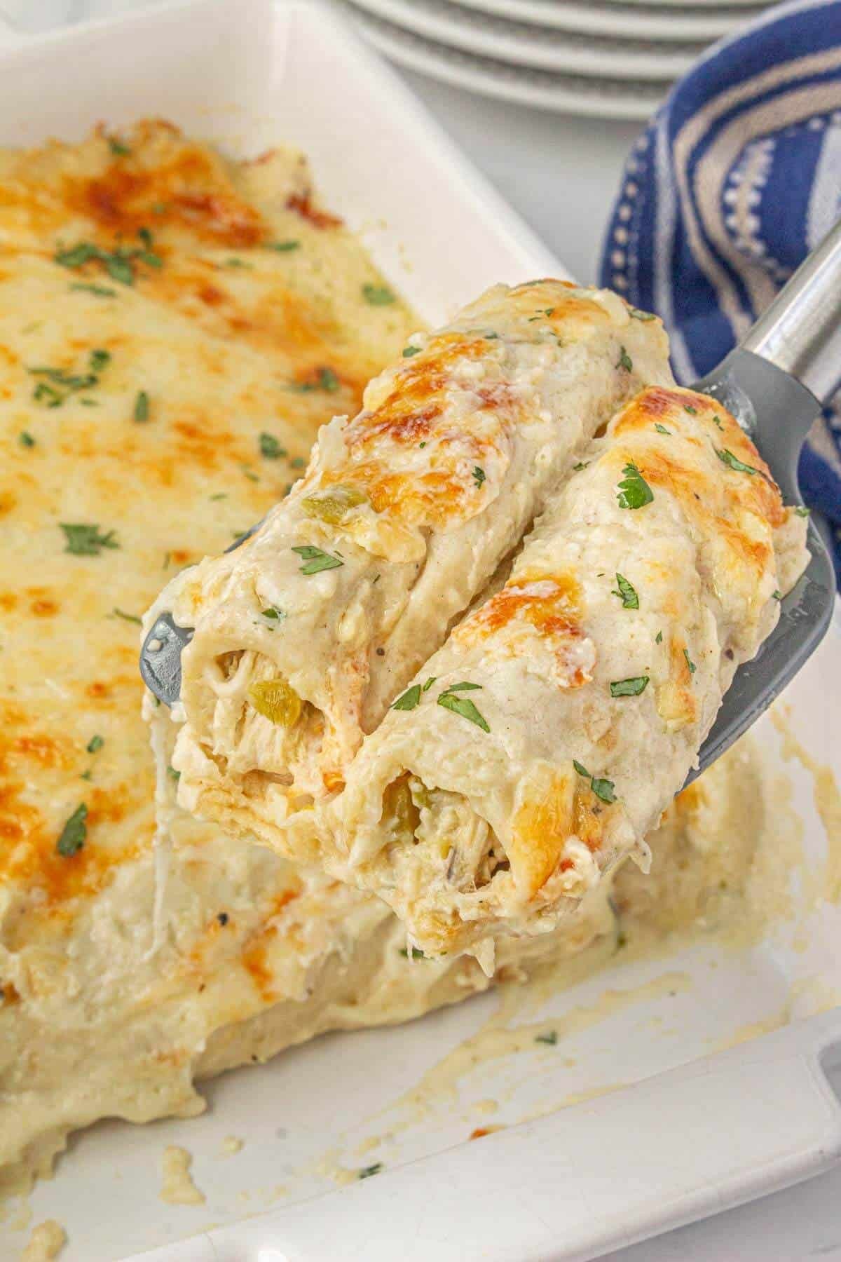 Close-up of golden brown creamy white chicken enchiladas in a baking dish, garnished with fresh cilantro and a dollop of sour cream.