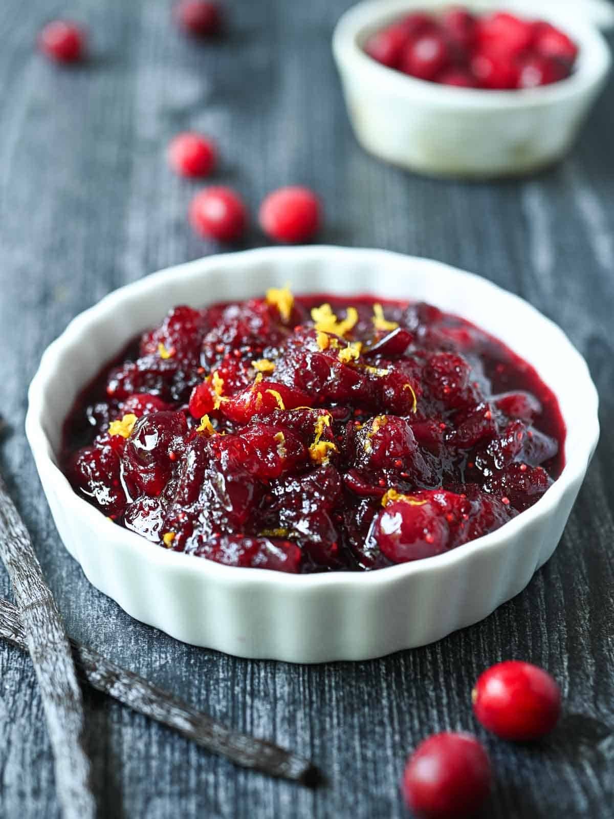 Vibrant homemade cranberry sauce in a rustic bowl with vanilla bean pod beside it