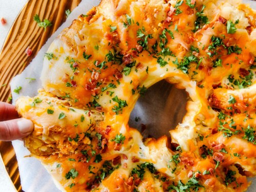 Close-up of cheesy spicy buffalo chicken pull-apart bread, golden brown, with blue cheese dip in the background on a rustic wooden board, perfect for a party.