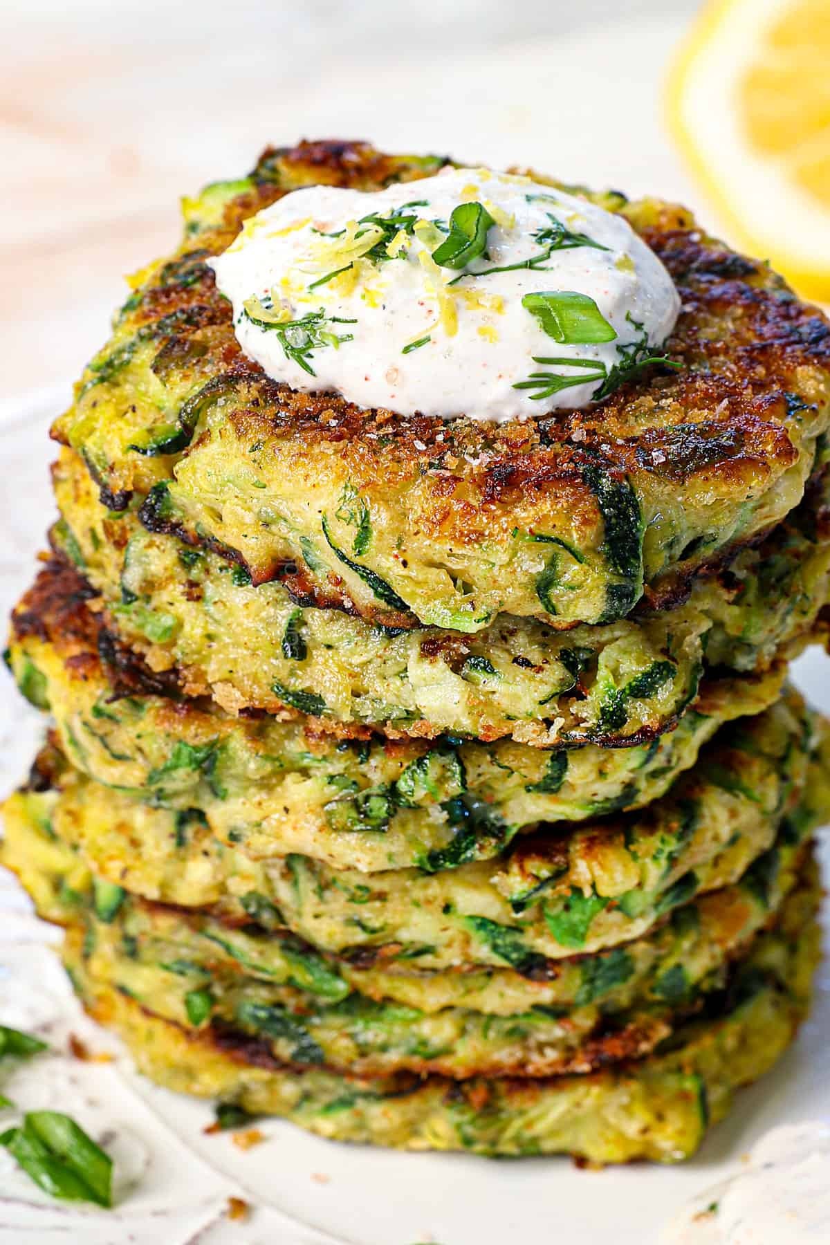 Crispy baked zucchini fritters stacked with a dollop of fresh herb yogurt, vibrant green herbs