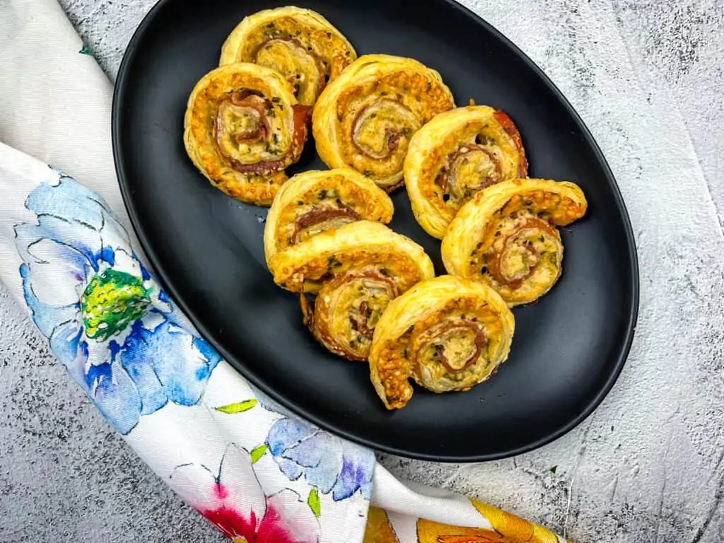 Assortment of savory puff pastry pinwheels on a party platter, close-up, guests reaching for food