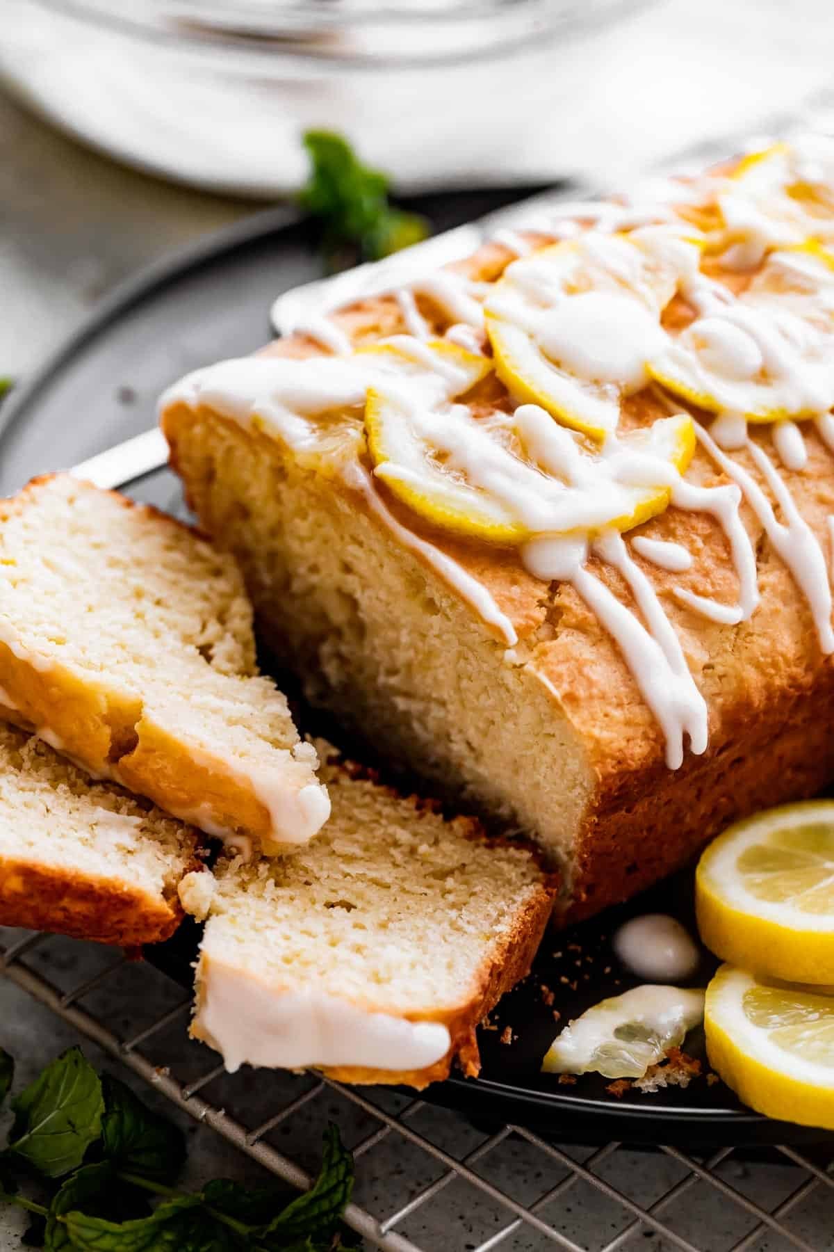 beautifully glazed lemon yogurt cake slice with a light, airy texture on a rustic wooden board, garnished with fresh lemon zest and mint