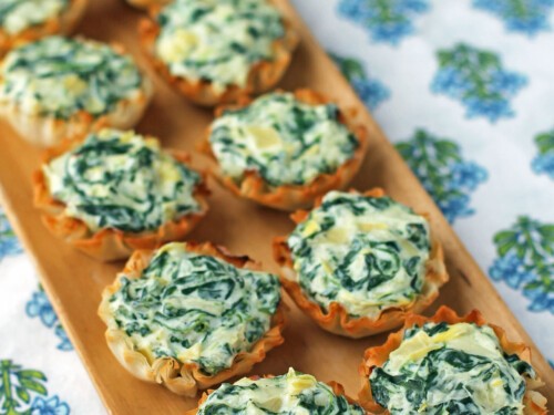 Spinach artichoke dip bites in mini phyllo cups on a party platter, close-up, golden brown, green specks, cheesy
