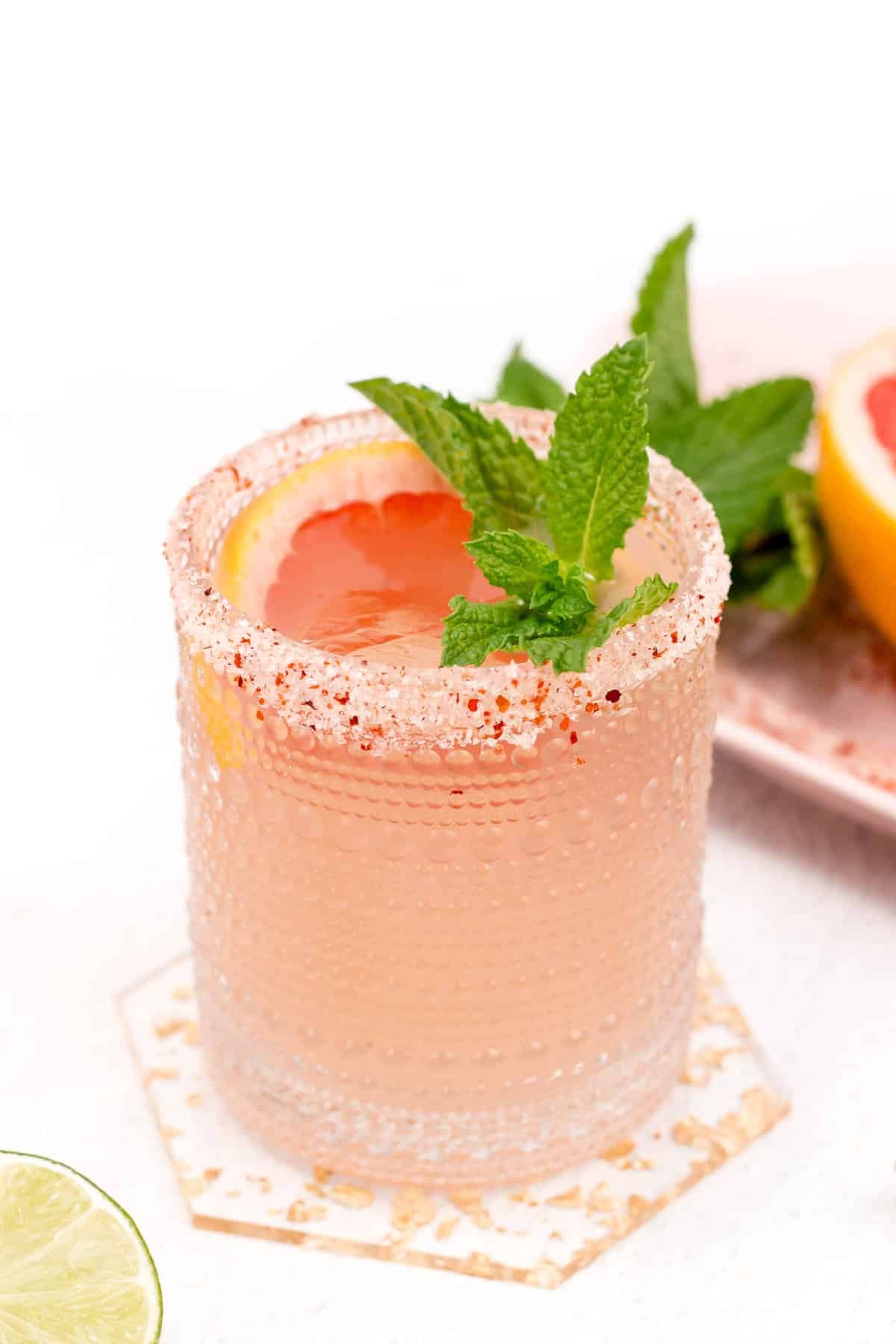 A refreshing pink cocktail with a salt rim, garnished with citrus and mint