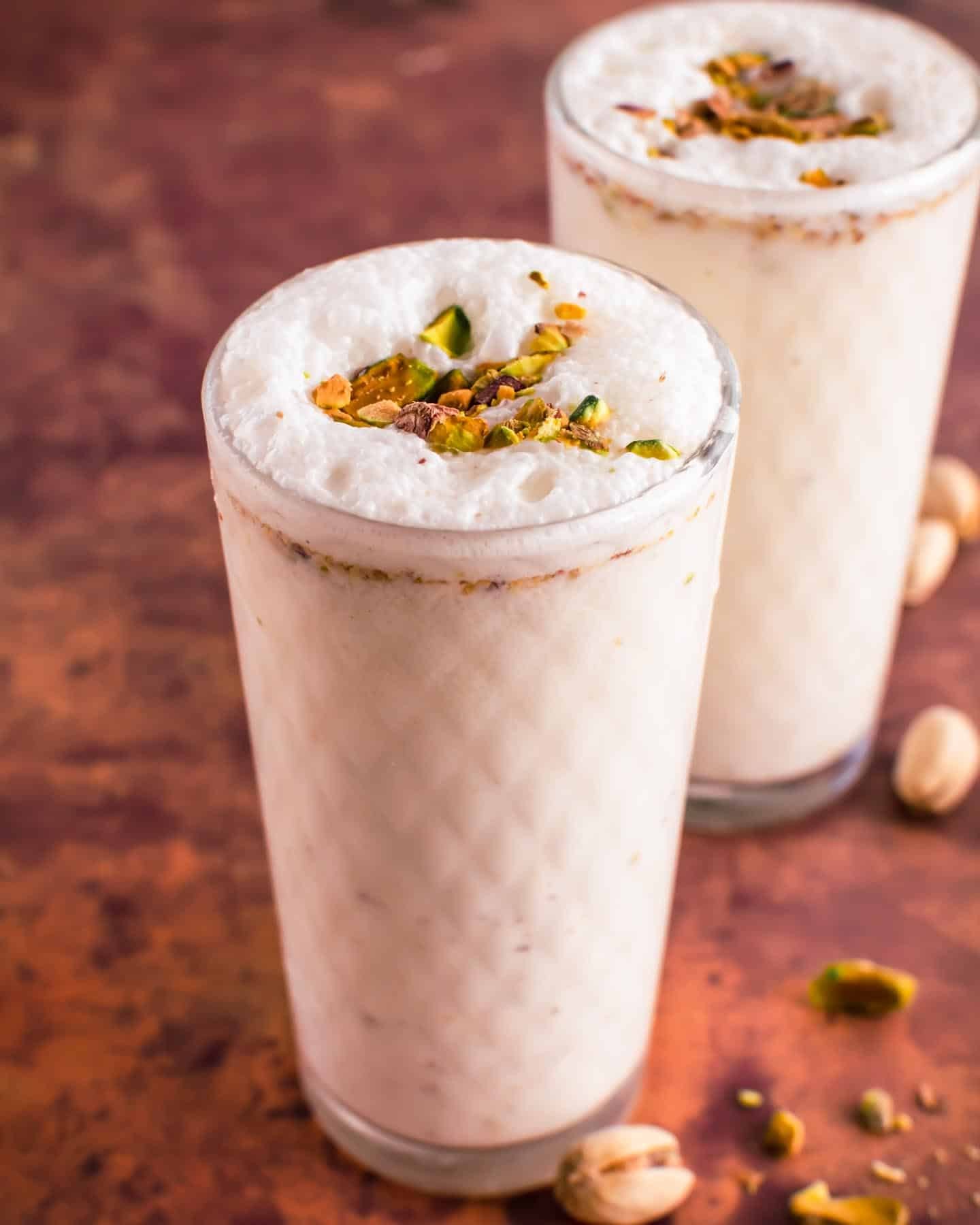 A vibrant glass of Pistachio Lassi topped with chopped pistachios and a mint sprig