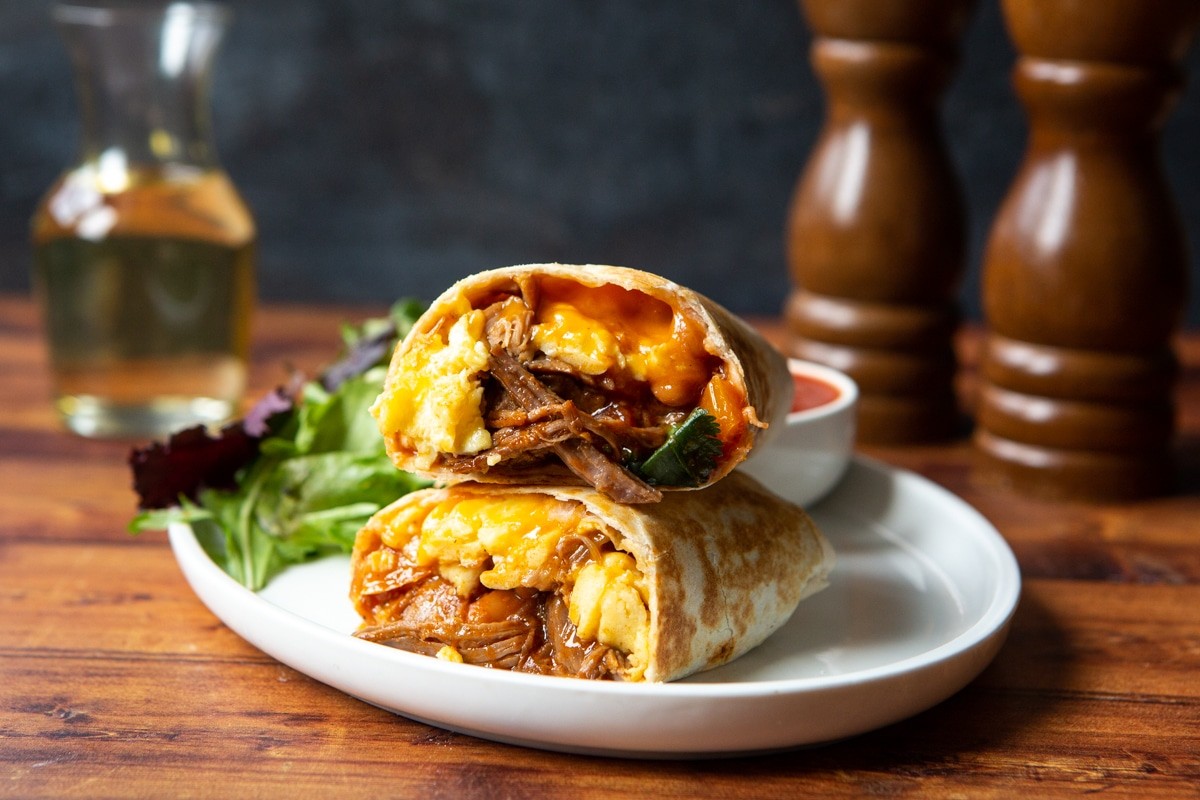 Coffee and cardamom spiced pulled pork breakfast burritos on a wooden cutting board, vibrant and appetizing presentation