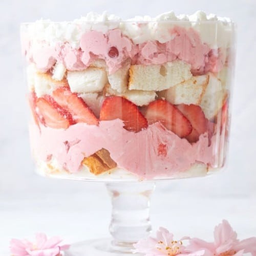 A vibrant and delicious strawberry trifle displayed in a glass trifle dish, showcasing layers of sponge cake, custard, strawberries, and whipped cream