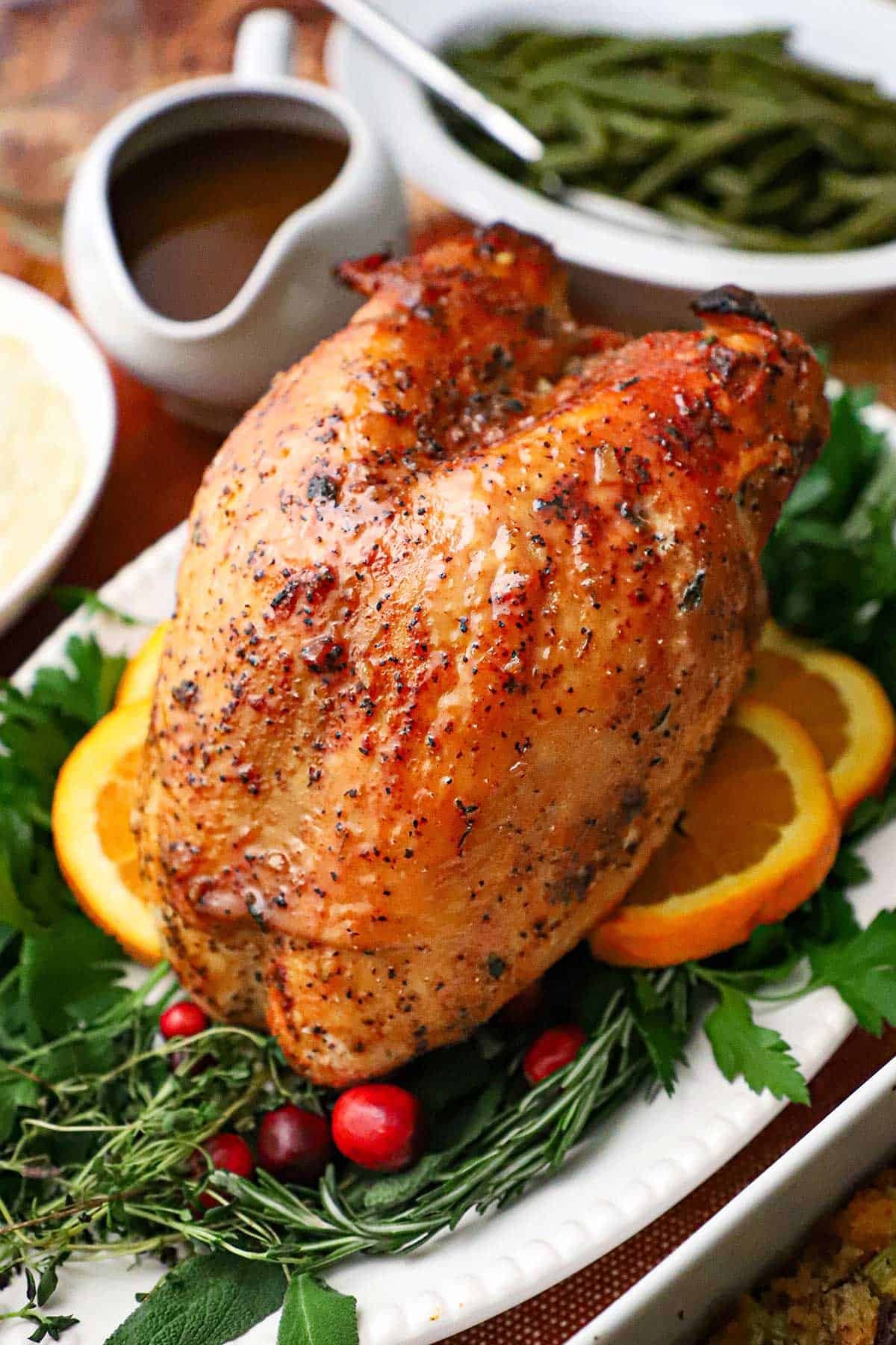 Golden brown maple glazed roast turkey with orange slices and fresh herbs on a festive platter