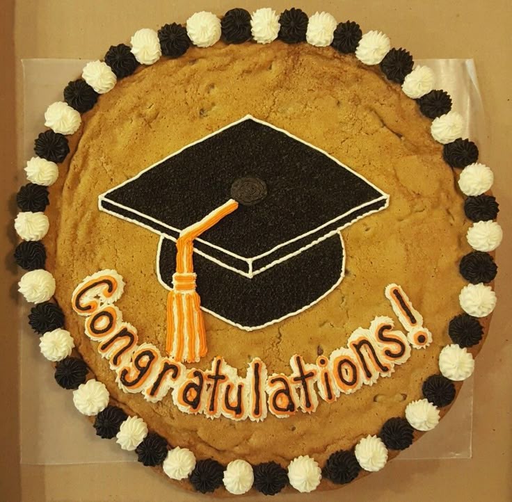 a beautifully decorated, large round cookie cake with 'Congrats Grad!' written in frosting, surrounded by graduation-themed decorations like caps and diplomas