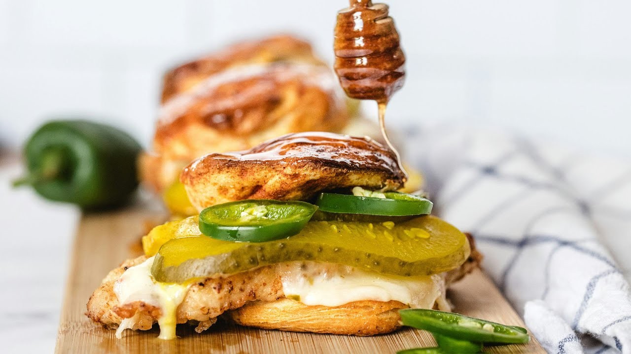Hot honey fried chicken biscuit sandwich with sweet heat drizzle, golden crispy chicken, fluffy biscuit, natural lighting, garnished with chives.