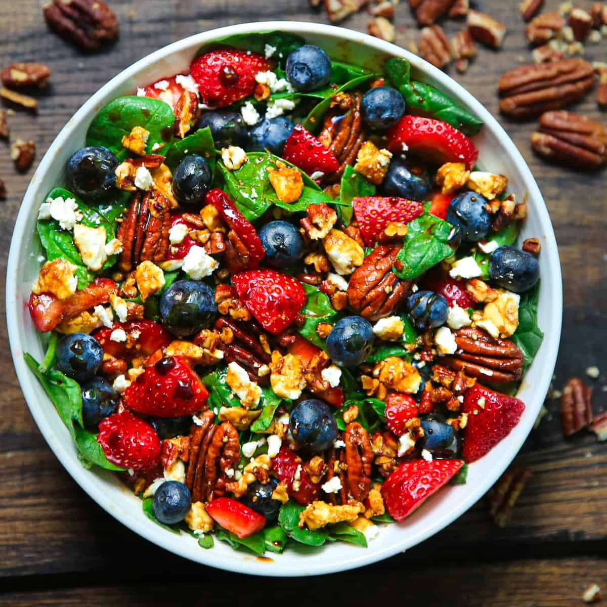 A vibrant strawberry spinach salad with crumbled cheese and nuts, drizzled with balsamic glaze