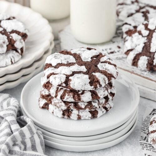 Plate of freshly baked chocolate crinkle cookies with powdered sugar and visible cracks, cozy kitchen background, warm lighting