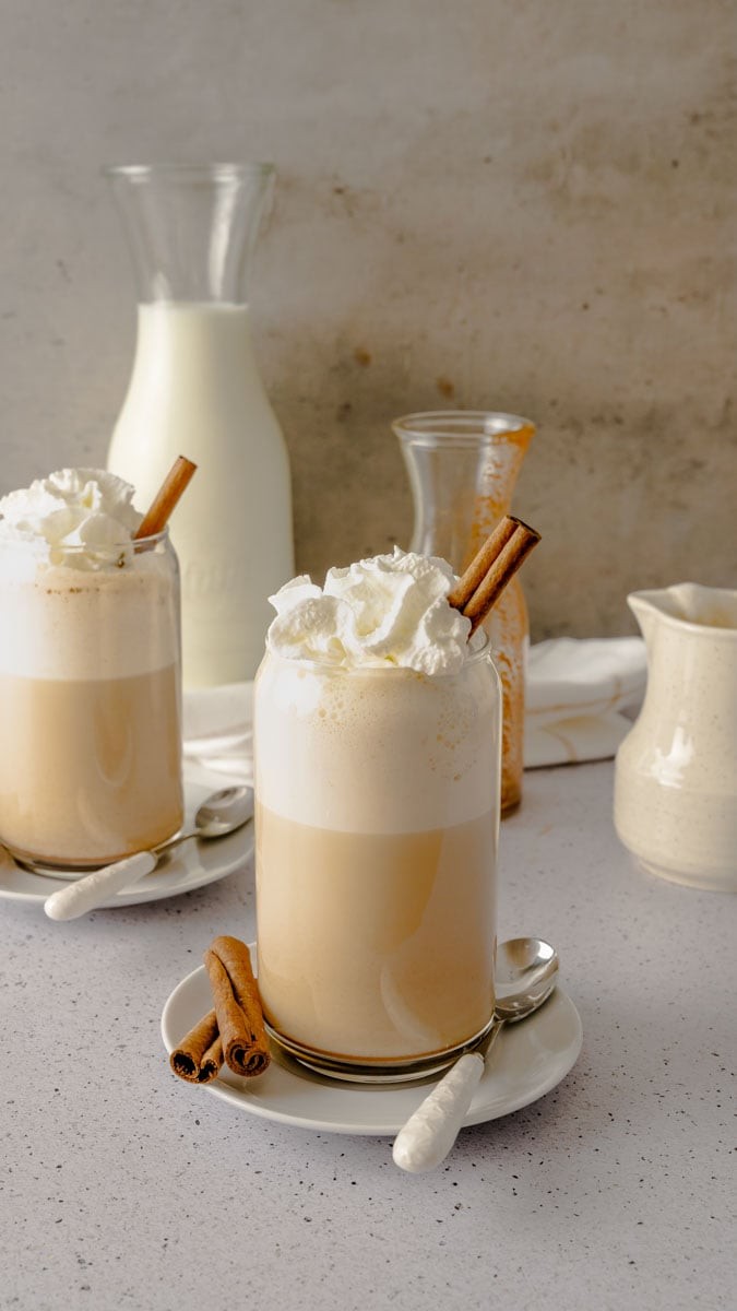 chai rocher latte in a clear glass mug with whipped cream and hazelnut garnish