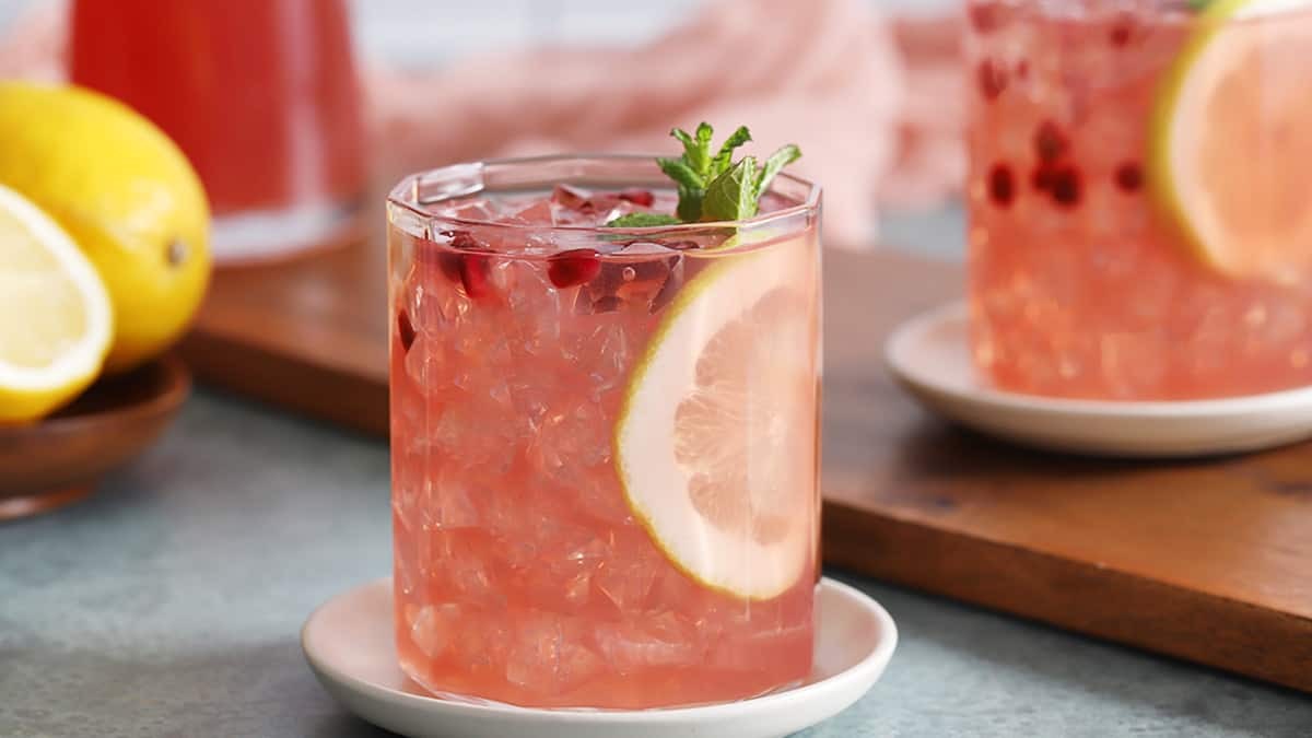 tall glass of pomegranate ginger lemonade garnished with a lemon slice and pomegranate seeds