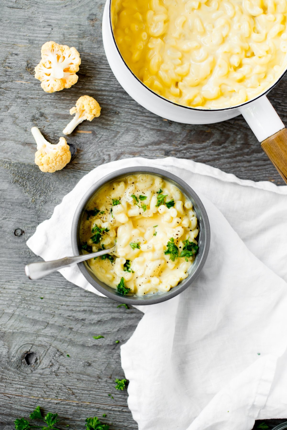 A bowl of creamy, golden cheesy cauliflower mac with a spoon, garnished with fresh parsley.