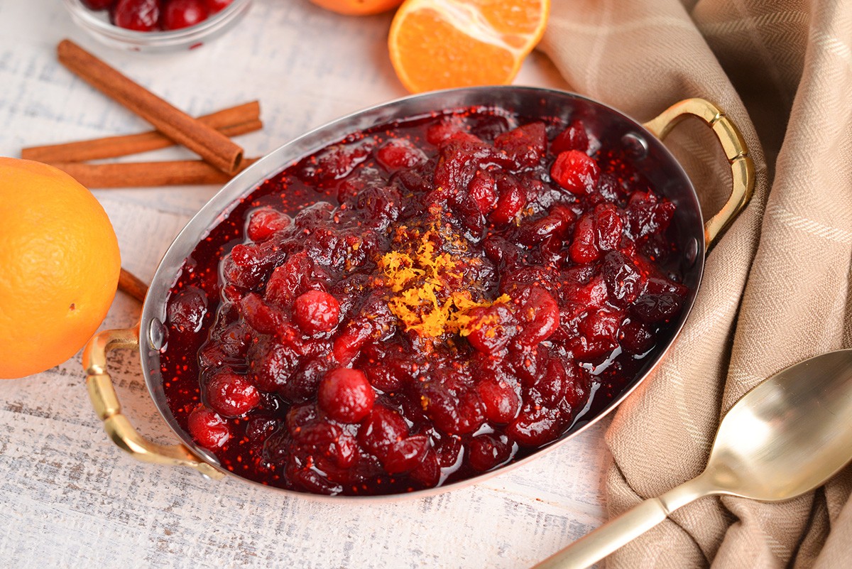 Vibrant homemade cranberry sauce simmering in a saucepan with orange zest, a festive holiday setting