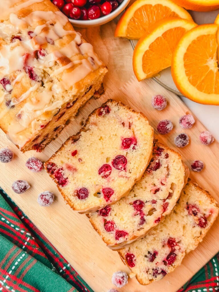 Vibrant cranberry orange bread loaf with shiny citrus glaze on a wooden cutting board, rustic kitchen setting
