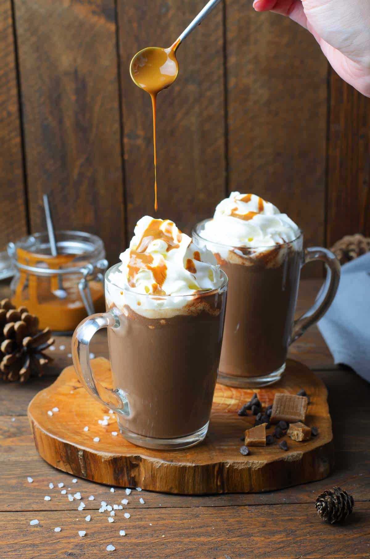 gourmet salted caramel hot chocolate with whipped cream and caramel drizzle in a cozy mug on a wooden table, warm lighting