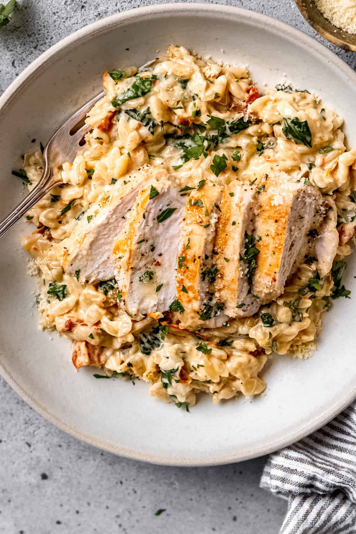 Tuscan chicken orzo in a shallow bowl with fresh basil and a rustic wooden background