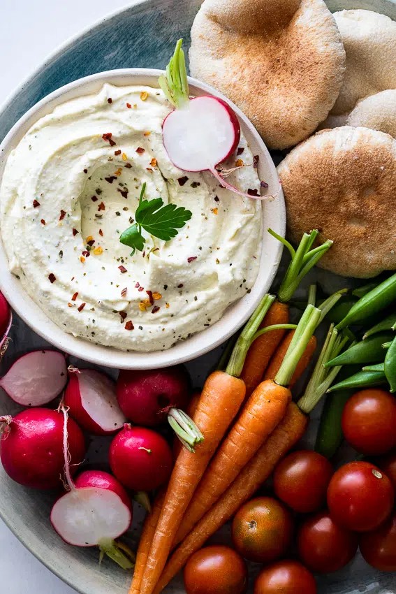 Vibrant spicy feta dip with fresh pita bread and colorful vegetables on a rustic wooden board, bright lighting