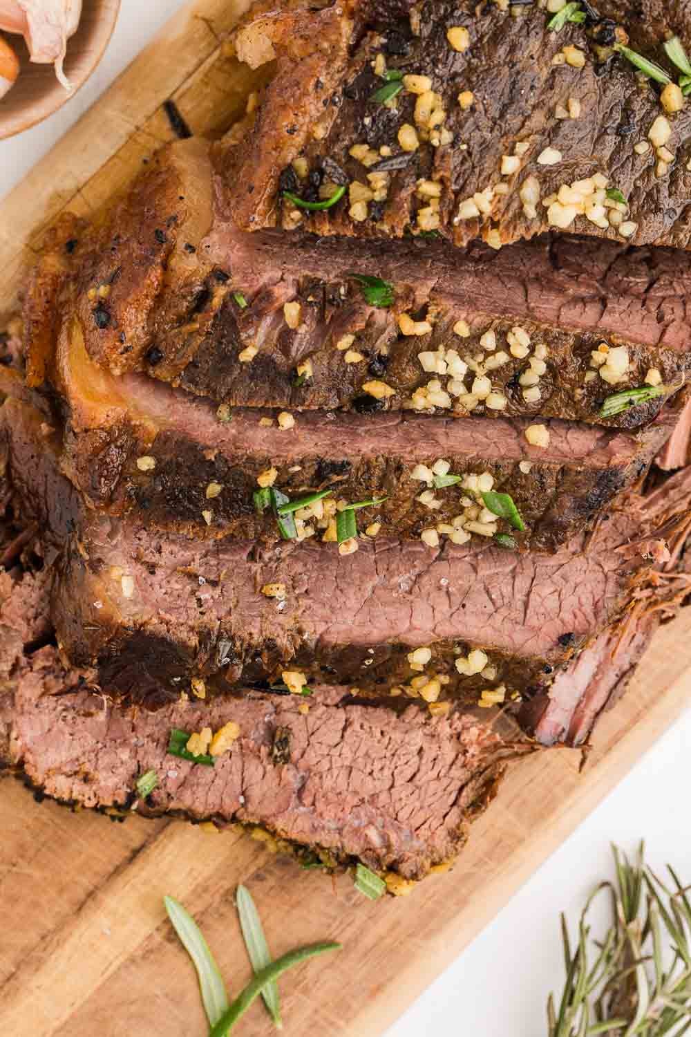 Close-up of a rustic chili-pepper beef roast, tender and juicy, on a cutting board with herbs