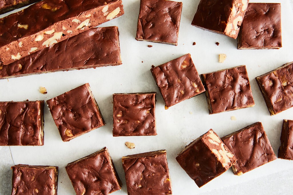 overhead shot of perfectly cut glossy chocolate fudge squares stacked on parchment paper, with a few cocoa nibs sprinkled on top
