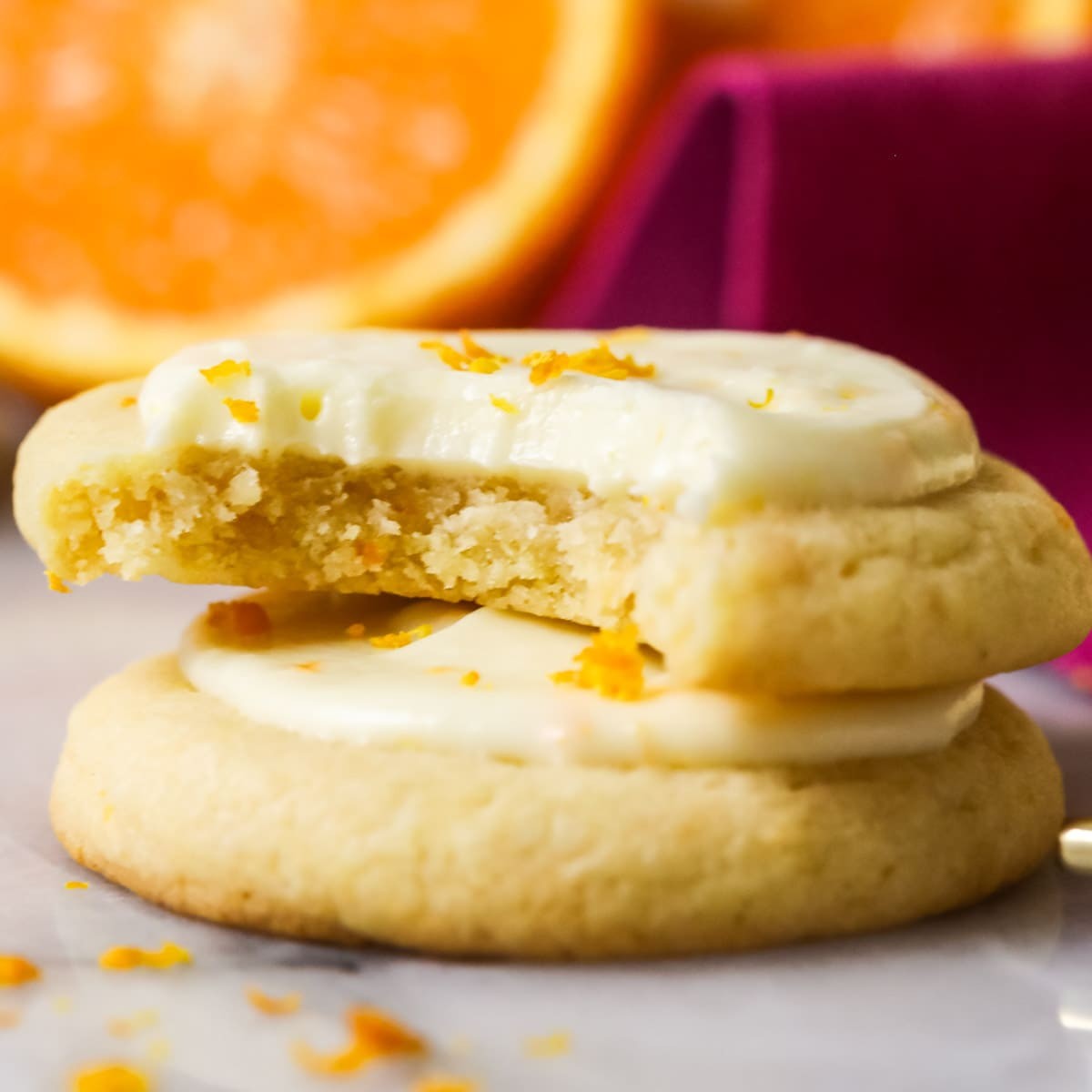 A close-up shot of perfectly baked orange zest cookies on a cooling rack, garnished with fresh orange slices and a dusting of powdered sugar.
