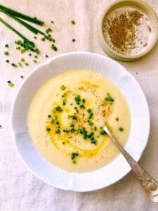 elegant bowl of creamy roasted cauliflower and leek soup, garnished with fresh chives, in a cozy kitchen setting with natural light