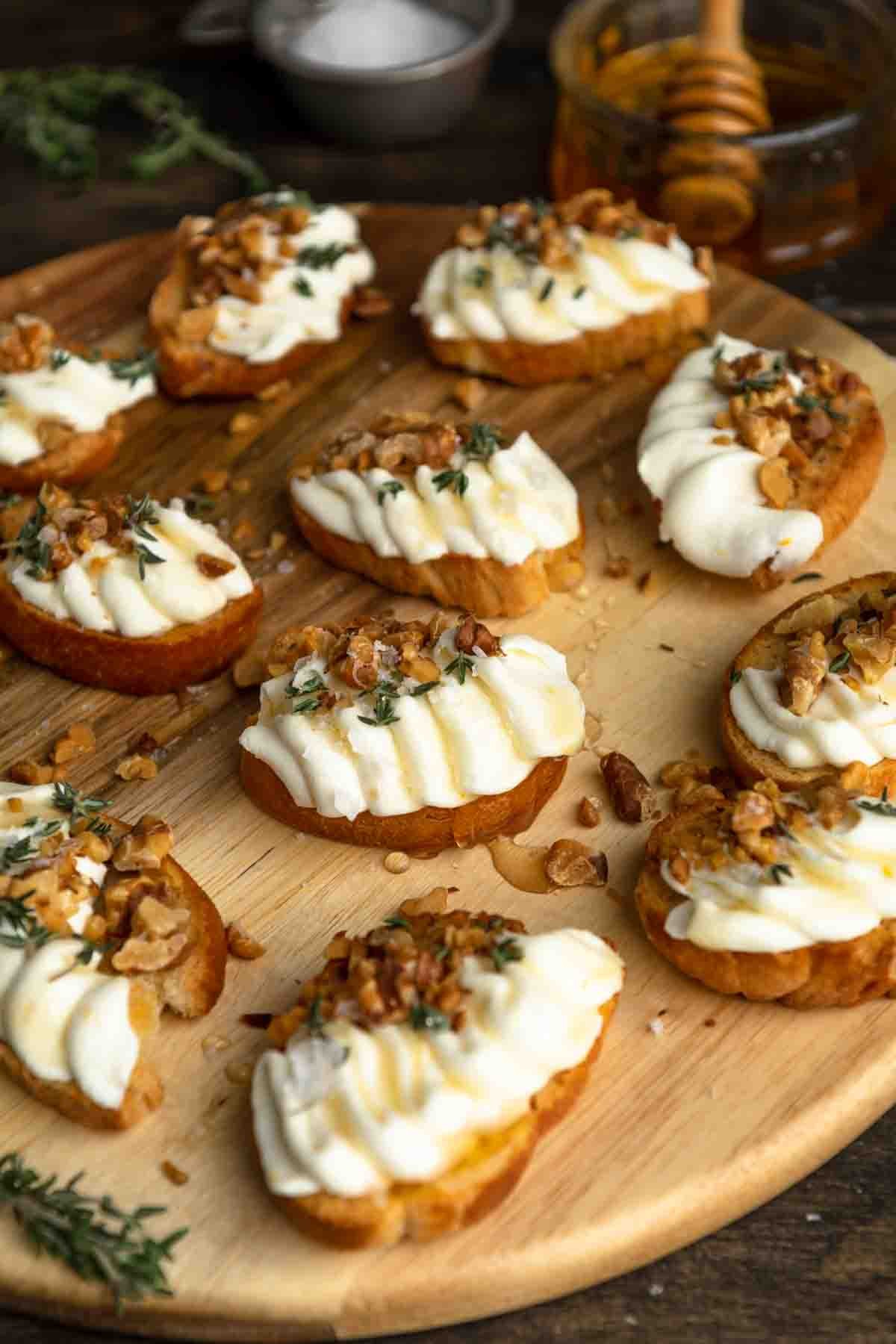Gourmet crispy crostini with fluffy whipped ricotta, drizzled with honey, garnished with fresh herbs, overhead shot on a rustic wooden board