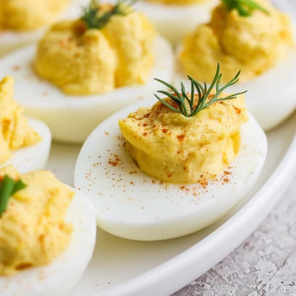 Platter of classic deviled eggs, garnished with paprika and fresh dill, bright lighting