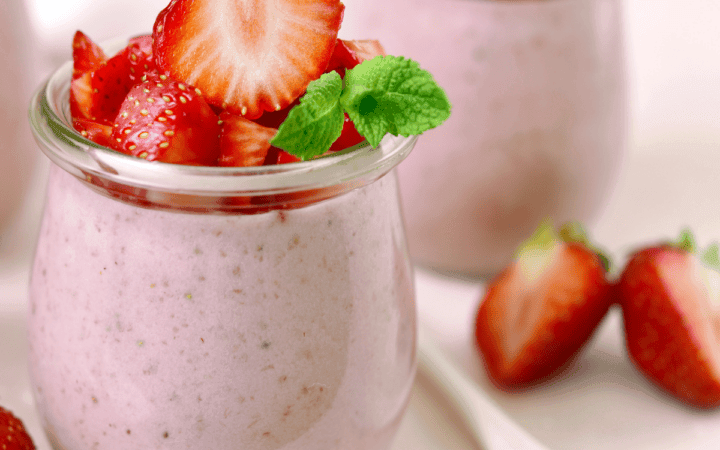a layered strawberry mousse dessert in a glass, garnished with fresh strawberries and mint